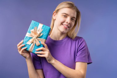 Violet 'in arka planında mutlu stil sahibi kadın hediye kutusu. Bayan gülümsüyor, içinde ne olduğunu merak ediyor. Hediye, sana bir sürprizim var. Yüksek kalite