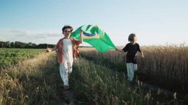 Brezilya 'lı küçük çocuklar. Futbol hayranı çocuklar yaz günbatımında ulusal bayrak altında koşuyorlar. Brezilya bayrağı, Amerika 'da tatiller. Yüksek kalite 4k görüntü