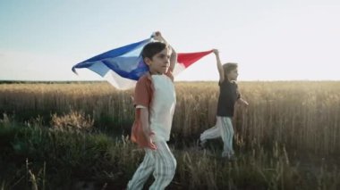 Fransız küçük çocukları. Vatansever çocuklar gün batımında ulusal bayrağıyla doğada koşuyorlar. Kutlama bayrağı, tatiller, Fransa, yeniden birleşme özgürlüğü günü. Yüksek kalite 4k görüntü