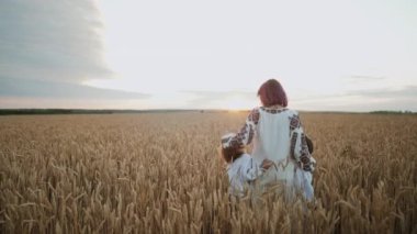 Küçük çocuklar ve anne gün batımında buğday tarlasında birlikte dururlar. Ukraynalı bir aile. Çocuklar bizim geleceğimiz. Oğulları olan bir kadın, kırsal kesimdeki çocuklar. Mutlu bir çocukluk. Yüksek kalite 4k görüntü