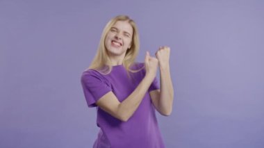 Güzel bir genç kadın zafer işareti gösterir. Zafer, başarılar, hedefler. Mutlu, mutlu, şaşırmış, mor arka plandaki mutlu bayan. Büyük ikramiye konsepti. Yüksek kalite 4k