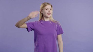 Dost canlısı genç kız el sallıyor. Merhaba, ya da hoşça kal, kaos, adios. Ayrılıyorum, kameraya hoşça kal de. Violet stüdyosundaki güzel bayan. Yüksek kalite 4k görüntü