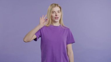 El işareti olan şık bir kadın. Tamam, jest yap. Mutlu bayan, doğru seçim, harika bir anlaşma, menekşe arkaplan. Pozitif kadın model kameraya gülümser, onay, güven konsepti. 4k kalite