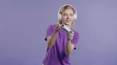 Violet stüdyosunun arka planında, joystick izole edilmiş video oyunu oynayan güzel genç bir kadın. Modern teknolojiyi kullanarak. E-spor, hobi, akış