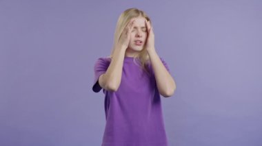 Acı çeken güzel bir genç kızın portresi baş ağrısı, menekşe stüdyo portresi. Kadın ellerini başının üstüne koyuyor. Migren sorunları, ilaç, hastalık, manyetik fırtınalar kavramı.