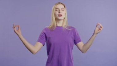 Sakin bir kadın dinleniyor, meditasyon yapıyor, stresi reddediyor. Sarışın kadın derin derin nefes alıyor, Violet stüdyo arka planını sakinleştiriyor. Yoga, ahlaki denge, zen konsepti. Yüksek kalite 4k