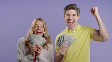 Amerikan doları olan inanılmaz bir kadın ve erkek. Genç Amerikalı çift, menekşe duvarında dolar banknotları tutuyor. Başarı, kazanç, maaş, fayda, yatırım sembolü.