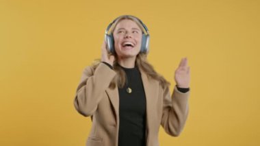 Mutlu iş kadını kafayı bulur, müzik dinler, sarı stüdyo arka planında kulaklıklarla dans etmekten zevk alır. Radyo, kablosuz modern ses teknolojisi, çevrimiçi çalar. Yüksek kalite 4k