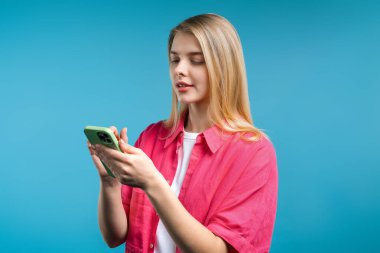 Akıllı telefondan internette sörf yapan güzel bir kadın. Mavi arka planda gülücük ve neşe dolu bir kız. Teknoloji, başarı, mutluluk, sosyal ağ konsepti. Yüksek kalite