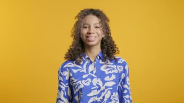 Mavi günlük kıyafetli muhteşem Afro-Amerikalı genç evet işareti veriyor, başını sallıyor, onaylıyor. Olumlu gülümseyen kız, vücut dili. Doğru mükemmel seçim, harika bir anlaşma. sarı stüdyo arka planı.
