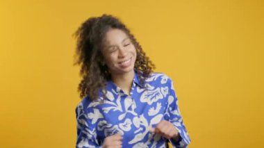 Komik, sevimli Afrikalı Amerikalı genç eğleniyor, en sevdiği müzik, gülümsüyor, sarı stüdyo arka planında dans ediyor. Müzik, dans konsepti, 4k