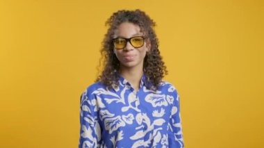 Sarı stüdyo arka planında kameraya gülümseyen, güneş gözlüklü Afro-Amerikan stil kızı. Romantik mavi tatil kıyafetli hoş bir bayan. Yüksek kalite 4k