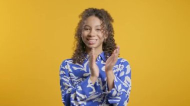 Sarı arka planda alkışlayan Afro-Amerikan genç kızı. Gülümseyen bayan el çırpıyor, tebrik ediyor. Destek, tezahürat, minnettarlık konsepti