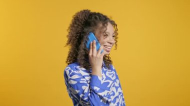Çekici, genç Afrikalı bir kadın telefonla konuşuyor, gülümsüyor. Sarı arka plandaki genç bayan. Genç kız akıllı telefon görüşmesi yapıyor. - Evet. Yüksek kalite 4k görüntü