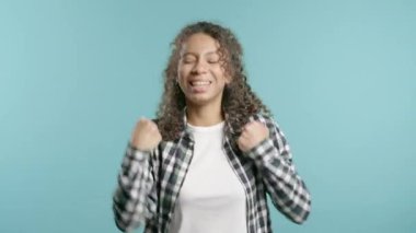 Güzel, Afro-Amerikan bir kadın zafer işareti gösteriyor. Evet, başarıyor. Hedeflerine ulaşıyor. Mutlu, mutlu, şaşırmış mavi arka plandaki mutlu bayan. Büyük ikramiye. Yüksek kalite 4k