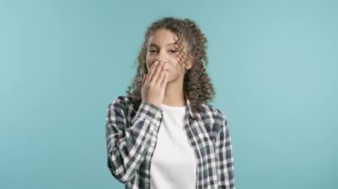 Çekici, Afro-Amerikalı, hipster giysili genç bir kadın mavi duvar arka planındaki kameraya hava öpücüğü yolluyor. Sevimli moda bayan portresi.