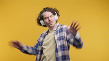 Pozitif hipster Amerikalı adam müzik dinliyor, sarı stüdyo arka planında modern kulaklıklarla dansın tadını çıkarıyor. Radyo, kablosuz modern ses teknolojisi, çevrimiçi çalar. Yüksek kalite 4k