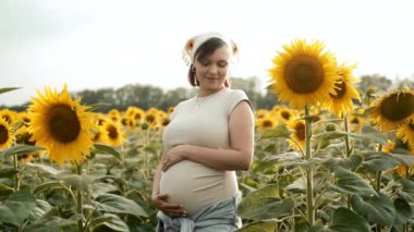 Müstakbel anne bebek bekliyor. Sağlık hamileliği, mutlu annelik. Hamile bir kadın göbeğini ayçiçeklerinin üzerinde okşuyor. Yüksek kalite 4k görüntü