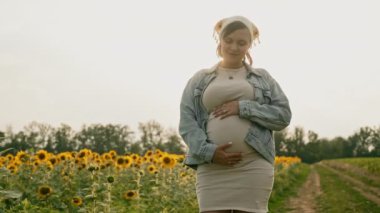 Mutlu hamile kadın dokunuyor, karnını okşuyor güneş batarken doğal tarla, altın saat. Hamilelik, annelik, annelik. Kadın vücudunun güzelliği. Yüksek kalite 4k görüntü