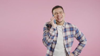 Gülümseyen Afro-Amerikan adam telefonla konuşuyor, güzel şaka, gülümsüyor. Pembe arka plandaki genç adam. Akıllı telefon görüşmesi. Yüksek kalite 4k 