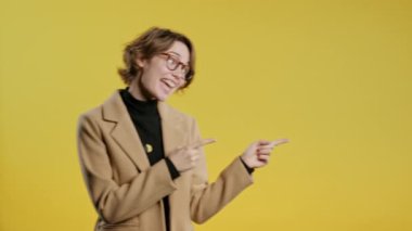 Gülümseyen 30 'lu yaşlardaki öğrenci bayan reklamınız için boş bir yer arıyor. Önerilen kadın sağ tarafı işaret ediyor, boşluğu kopyalayın. Kadın, izole edilmiş sarı bir arka plan sunuyor. Yüksek kalite