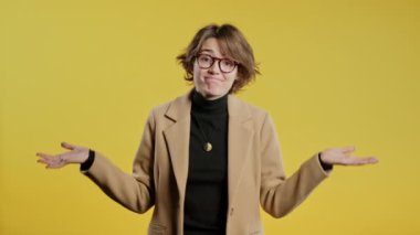 Kafası karışmış güzel bir iş kadını ya da öğrenci, omuzları kalkık, yardımcı olamıyor, bilmediğim hareketler yapıyor. Zor soru, suçlu tepkisi, sarı arka planda şaşkın stil sahibi bir kadın. Yüksek kalite 4k