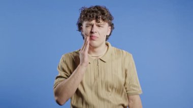 Mavi stüdyo geçmişinde diş ağrısı olan yakışıklı kıvırcık saçlı bir adam. Diş ağrısı, diş sorunları, diş hekimliği ve tıp konsepti