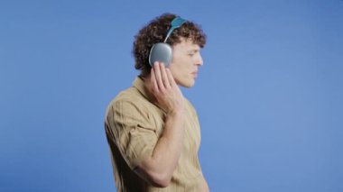 Müzik dinleyen yakışıklı bir adam. Mavi stüdyo arka planında modern kulaklıklarla dansın tadını çıkarıyor. Radyo, kablosuz modern ses teknolojisi, çevrimiçi çalar. Yüksek kalite 4k