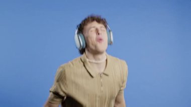 Pozitif Amerikalı adam müzik dinliyor, mavi stüdyo arka planında modern kulaklıklarla dansın tadını çıkarıyor. Radyo, kablosuz modern ses teknolojisi, çevrimiçi çalar. Yüksek kalite 4k