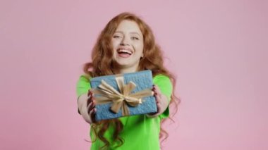 Pembe arka planda mutlu, kızıl saçlı kadın hediye kutusu. Genç kız gülümsüyor, kameraya hediye veriyor. Sana bir sürprizim var. Yüksek kalite 4k