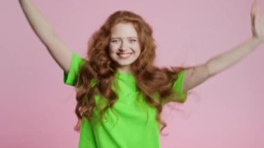 20 'li yaşlarda kızıl saçlı komik bir kadın eğleniyor, en sevdiği müzik çalıyor, gülümsüyor, pembe stüdyo arka planında dans ediyor. Müzik, dans konsepti. Yüksek kalite 4k görüntü