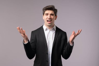 Sinirli iş adamı kamerayı gösteriyor ve ne jesti gösteriyor. Deli misin diye soruyorum. Tartışan patron yönetici gri arka planda izole edildi. Öfkeli ifade, birini suçlamak..