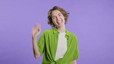 Dost canlısı genç bayan el sallıyor - merhaba, ya da selam, kao, adios. Ayrılıyorum, kameraya hoşça kal de. Violet stüdyosundaki güzel bayan. Yüksek kalite 4k