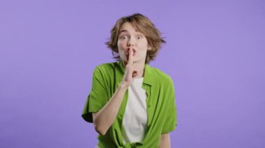 Dudağında parmak tutan güzel, şık bir kadın, Violet stüdyo arka planı. Sessiz olun, sessiz olun, komplo kurun, dedikodu yapın, dedikodu yapın. Yüksek kalite 4k