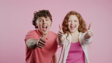 Havalı bir kadın ve el işareti olan bir erkek, iyi niyet göstergesi. Mutlu çift, doğru seçim, harika bir anlaşma, pembe arka plan. Pozitif arkadaşlar kameraya gülümser, onay, güven konsepti. 4k