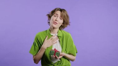 Violet 'in arka planında mutlu stil sahibi kadın hediye kutusu. Gülümseyen bir bayan, içinde ne olduğunu merak ediyor. Hediye, sana bir sürprizim var. Yüksek kalite 4k