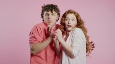 Korkmuş beyaz Amerikalı çift bir şeyden korkuyor ve pembe duvarda korku dolu büyük gözlerle kameraya bakıyor. Kızıl saçlı kadın ve erkek. Yüksek kalite 4k görüntü