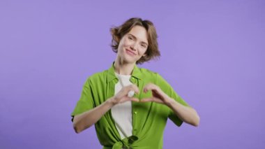 Gülümseyen kadın kalbinin şeklini gösteriyor. Menekşe rengi pozitif kadın. Sevgi. Kadın sağlığı, gönüllülük, bağış, minnettarlık sembolü, flört konsepti. Yüksek kalite 4k görüntü