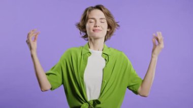 Sakin kadın rahatlıyor, meditasyon yapıyor, stresi reddediyor. Kadın derin nefes alıyor, Violet stüdyosunun arka planını sakinleştiriyor. Yoga, ahlaki denge, zen konsepti. Yüksek kalite 4k