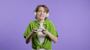 Violet stüdyosunun arka planında, joystick izole edilmiş video oyunu oynayan güzel genç bir kadın. Modern teknolojiyi kullanarak. E-spor, hobi, akış