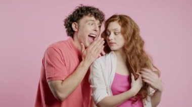 Dedikoducu adam kız arkadaşlarına fısıldıyor. Kulak sırrı, söylentiler, dedikodular, pembe stüdyo. Güzel bayan ve yakışıklı adam. Komplo konsepti. Yüksek kalite 4k