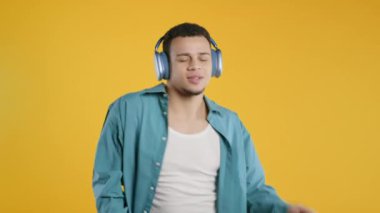 Pozitif Afro-Amerikalı adam müzik dinliyor, sarı stüdyo arka planında modern kulaklıklarla dansın tadını çıkarıyor. Radyo, kablosuz modern ses teknolojisi, çevrimiçi çalar. Yüksek kalite 4k