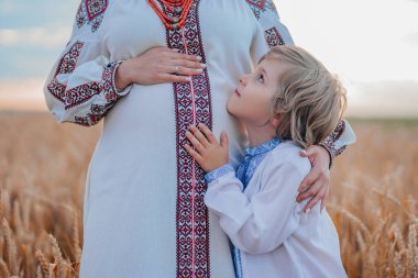 Doğadaki buğday tarlasında oğlu olan hamile Ukraynalı anne. Gülümseyen kardeş annelerin karnına dokunuyor. Aile yeni doğan bebeği bekliyor. Ukrayna 'da demografi. Yüksek kalite fotoğraf.