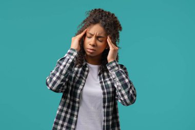 Afro-Amerikan güzel, acı çeken genç kızın portresi baş ağrısı, mavi stüdyo portresi. Kadın ellerini başının üstüne koyuyor. Migren sorunları, ilaç, hastalık, manyetik fırtınalar kavramı