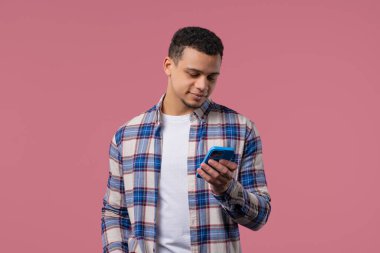 Akıllı telefondan internette sörf yapan yakışıklı bir erkek. Pembe arka planda gülücük ve neşe dolu bir adam. Teknoloji, başarı, mutluluk, sosyal ağ konsepti. Yüksek kalite