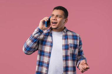 Gülümseyen Afro-Amerikan adam telefonla konuşuyor, güzel şaka, gülümsüyor. Pembe arka plandaki genç adam. Akıllı telefon görüşmesi. Yüksek kalite 