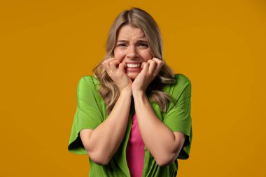 Bir şeyden korkan kadın, sarı arka planda şoka girmiş. Kafa tutmak, çığlık atmak. Yüksek kalite