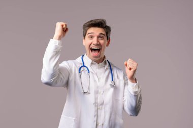 Beyaz önlük giymiş olgun bir doktor zafer işareti sergiliyor. Sonuç elde etti, hedeflerine ulaştı. Sağlık uzmanı mutlu, mutlu, şaşırmış, mutlu, mutlu, mutlu. Yüksek kalite