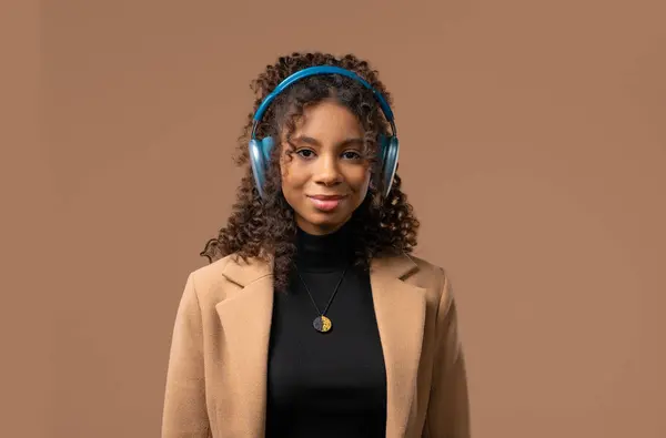 stock image Happy african american woman gets high, listening music, enjoying dance with headphones on beige studio backdrop. Radio, wireless modern sound technology, online player. High quality