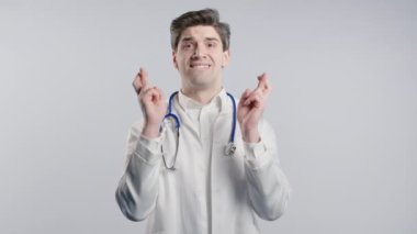 30 'lu yaşlarda beyaz önlüklü bir doktor beyaz arka planda dua ediyor. Birine arzularını tatmin etmesi için yalvarır, yardım eder, şans için dua eder. Yüksek kalite 4k görüntü